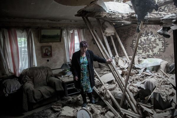 Junio de 2014. Una vecina del pueblo de Golubovka, en la región de Donetsk, pasa por su casa tras el bombardeo de las Fuerzas Armadas de Ucrania. - Sputnik Mundo