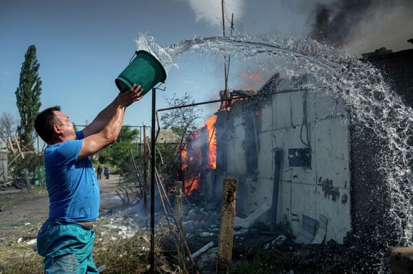 Julio de 2014. Aldea Lugánskaia. Un residente local apaga una casa que se incendió tras un ataque aéreo. - Sputnik Mundo