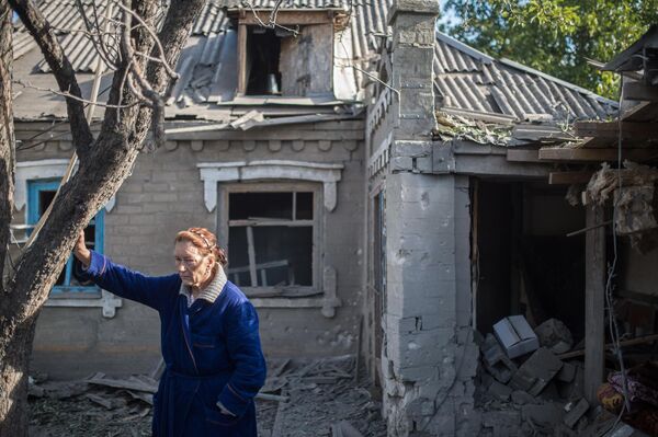 Agosto de 2015. Una mujer frente a una casa dañada por los bombardeos ucranianos en el pueblo de Aleksándrovka, en la región de Donetsk. - Sputnik Mundo