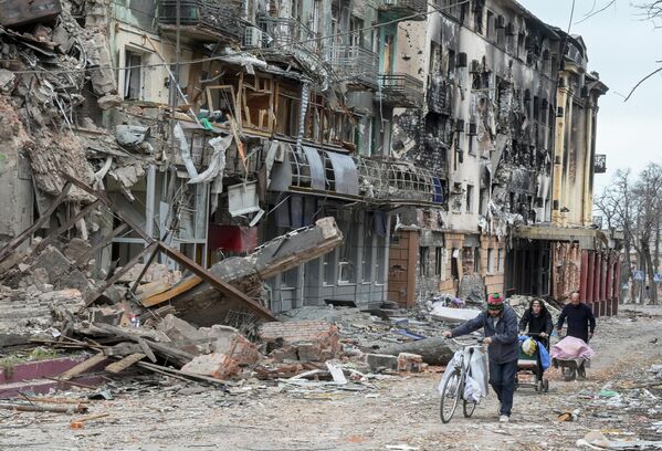 Los habitantes de la ciudad ucraniana de Mariúpol caminan por una calle al lado de los edificios destruidos. - Sputnik Mundo
