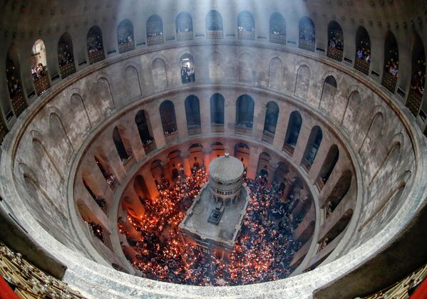 Los cristianos ortodoxos se reúnen con velas encendidas alrededor del Edículo, tradicionalmente considerado como el lugar de enterramiento de Jesucristo, durante la ceremonia del Fuego Sagrado en la iglesia del Santo Sepulcro de Jerusalén. 23 de abril de 2022. - Sputnik Mundo