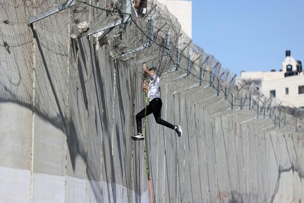 Un adolescente desciende al barrio árabe de Beit Hanina, en Jerusalén Este, con una cuerda atada a un muro de hormigón de ocho metros levantado por los israelíes que separa Israel de Cisjordania. - Sputnik Mundo