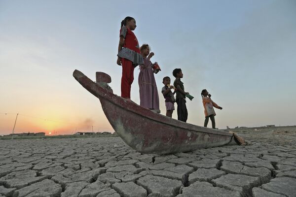Unos niños parados sobre un bote que yace en el lecho seco de lo que era el pantano de Chibayish, en Irak. 24 de julio del 2022. - Sputnik Mundo