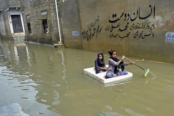 Dos niñas navegan sobre una balsa improvisada por las calles de la ciudad pakistaní de Karachi tras las intensas lluvias. 26 de julio del 2022. - Sputnik Mundo