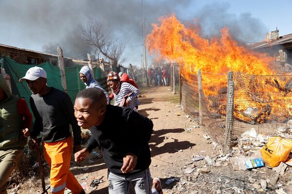 Los habitantes de un municipio cerca de Randfontein, en Sudáfrica, huyen de un albergue en llamas. Ese lugar estaba supuestamente ocupado por mineros ilegales y fue incendiado durante las protestas locales contra la minería ilegal. - Sputnik Mundo