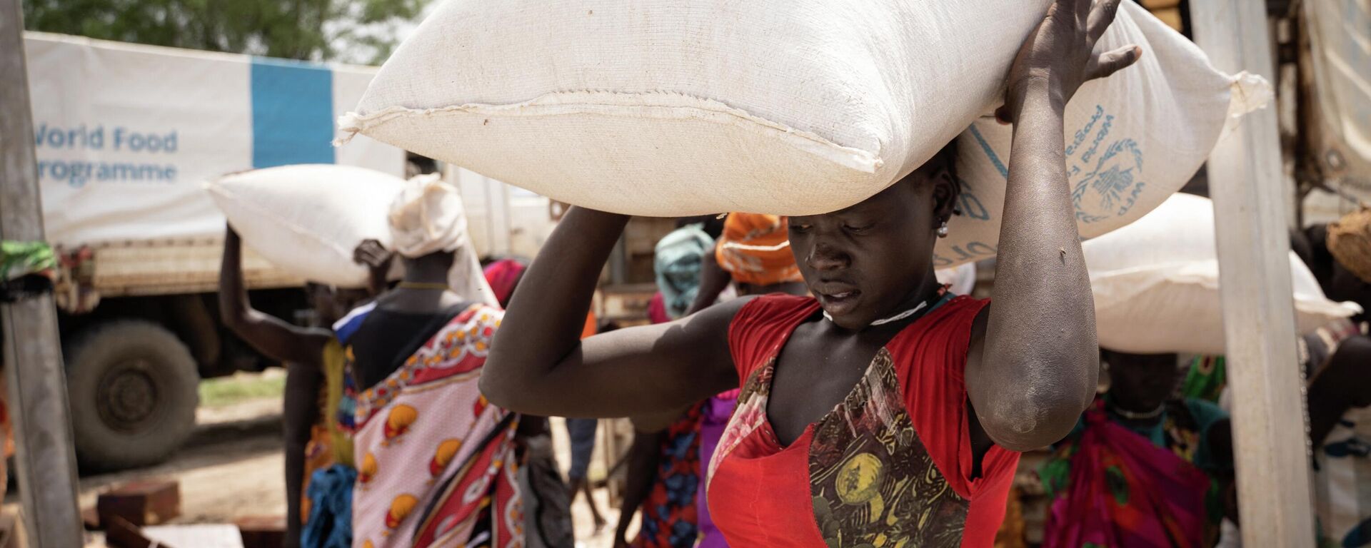 Mujeres llevan bolsas de sorgo durante una distribución de alimentos del Programa Mundial de Alimentos (PMA) de las Naciones Unidas en Gumuruk, Sudán del Sur - Sputnik Mundo, 1920, 03.11.2022