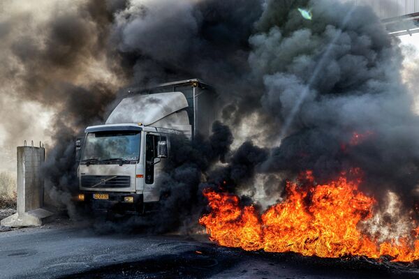 Un camión que se dirigía a la ciudad palestina de Nablus pasa con neumáticos ardiendo por el puesto de control de Hawara. - Sputnik Mundo