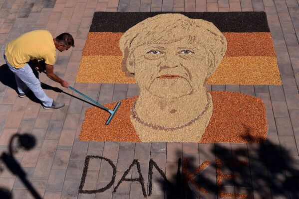 En vísperas de la dimisión de la canciller alemana Angela Merkel el artista kosovar Alkent Pozhegu completa su retrato en la plaza de la ciudad de Gjakova, creándolo con semillas y granos. - Sputnik Mundo
