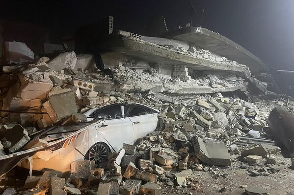 Un auto bajo los escombros de un edificio derrumbado en la ciudad de Azmarin, en la provincia de Idlib, en el norte de Siria. - Sputnik Mundo