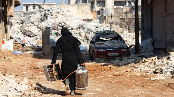 Mujer rescata una pequeña estufa y una bombona de gas, en la ciudad siria de Jindayris, Alepo controlada por los rebeldes, el 10 de febrero de 2023  - Sputnik Mundo