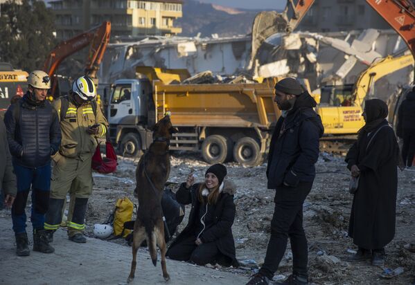 Una mujer juega con un perro de servicio en el lugar de una operación de búsqueda y rescate en Antakya. - Sputnik Mundo