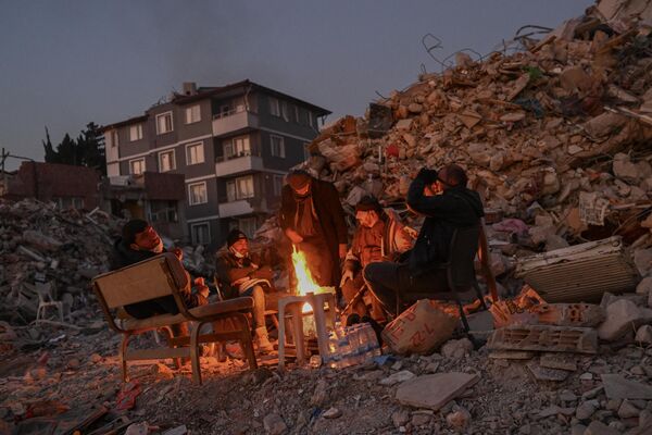 Residentes de la ciudad turca de Hatay se reúnen en torno a una hoguera cerca de un edificio de apartamentos destruido, donde sus seres queridos permanecen bajo los escombros. - Sputnik Mundo