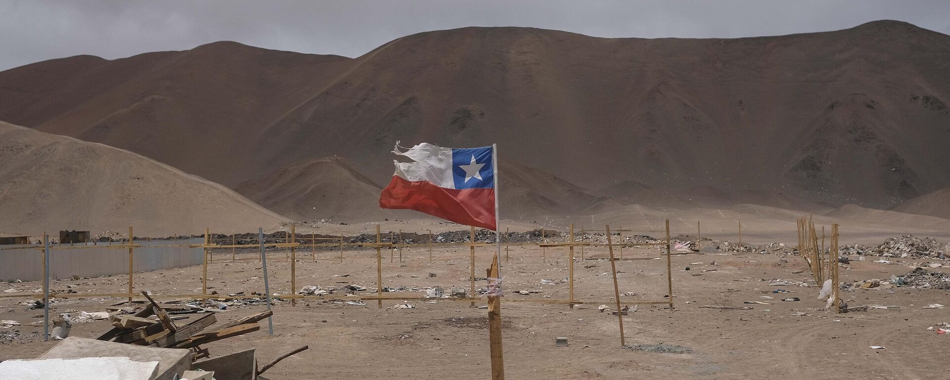 Una bandera chilena ondea en un poste de madera en un terreno donde se concentran los migrantes en Chile. - Sputnik Mundo, 1920, 27.02.2023