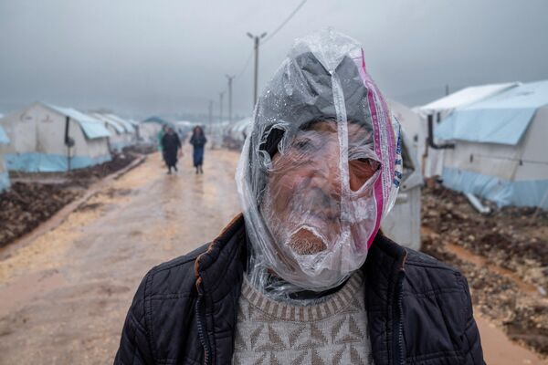Un hombre con una bolsa de plástico para protegerse de la lluvia camina por una carretera embarrada junto a tiendas de campaña instaladas para albergar a personas desplazadas tras los fuertes terremotos en Adiyaman, al sureste de Turquía. - Sputnik Mundo