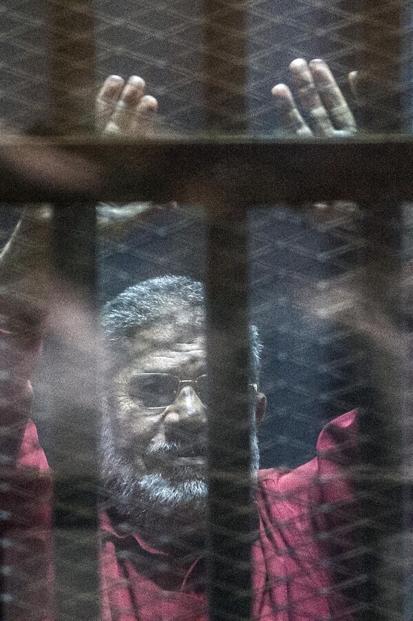 Mohamed Morsi, presidente islamista derrocado de Egipto, con uniforme rojo, gesticula desde los barrotes durante un juicio en la capital egipcia, en la academia de policía de El Cairo, el 23 de abril de 2016. Derrocado durante un golpe de Estado en 2013, Morsi fue juzgado por varios cargos, como incitar a sus partidarios a matar a manifestantes de la oposición. Falleció en 2019 tras sufrir un colapso en el tribunal donde se le juzgaba por cargos de espionaje. - Sputnik Mundo