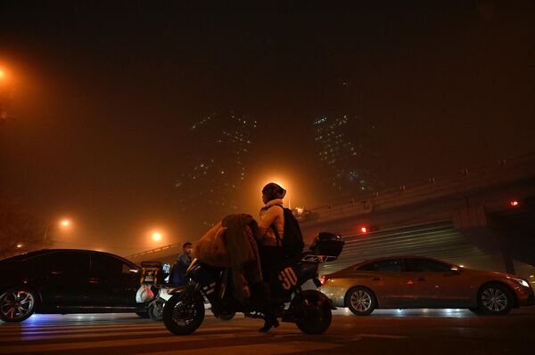 Una mujer monta en scooter en el centro de negocios de Pekín durante una tormenta de arena. - Sputnik Mundo