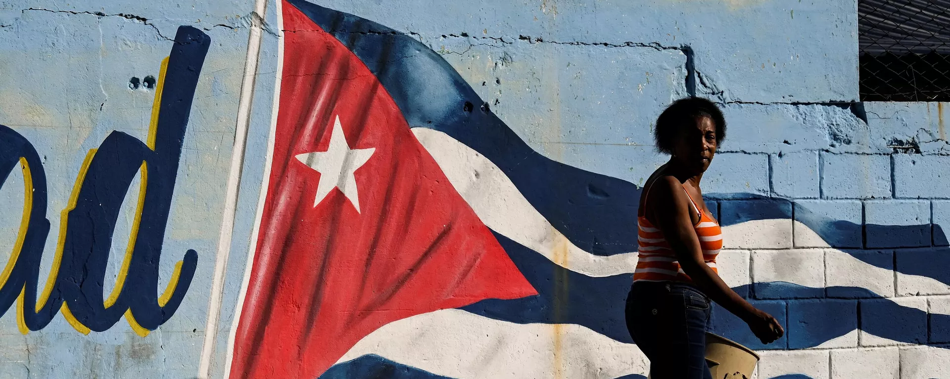 Una mujer pasa junto a un muro pintado con la bandera cubana con la leyenda Continuidad en La Habana, el 7 de febrero de 2023.  - Sputnik Mundo, 1920, 24.04.2024