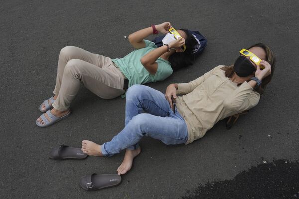 Los eclipses de ese tipo son bastante raros y se producen aproximadamente una vez cada década.En la foto: la gente se tumba en el suelo mientras usa gafas protectoras para ver el eclipse solar en Yakarta, Indonesia. - Sputnik Mundo