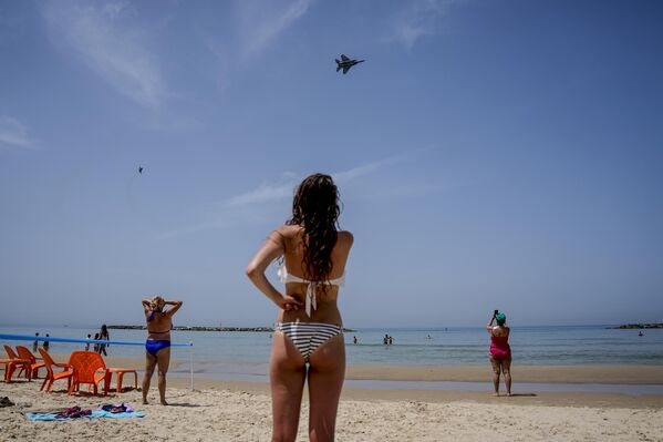 Unos veraneantes observan cómo dos cazas israelíes F-15 sobrevuelan la playa durante un ensayo para un desfile aéreo con motivo del 75 aniversario de la independencia de Israel. - Sputnik Mundo