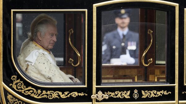 El rey Carlos III del Reino Unido y Camilla, la reina consorte, pasean en el carruaje de Estado del Jubileo de Diamante frente al Palacio de Westminster, de camino a su ceremonia de coronación, en Londres, el sábado 6 de mayo de 2023 - Sputnik Mundo