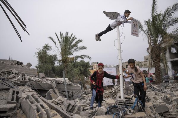 Niñas palestinas ante la imagen de un adolescente palestino muerto instalada sobre las ruinas de un edificio residencial destruido en Deir al-Balah, en el marco de la exposición &quot;La ocupación mata a la infancia&quot;. - Sputnik Mundo