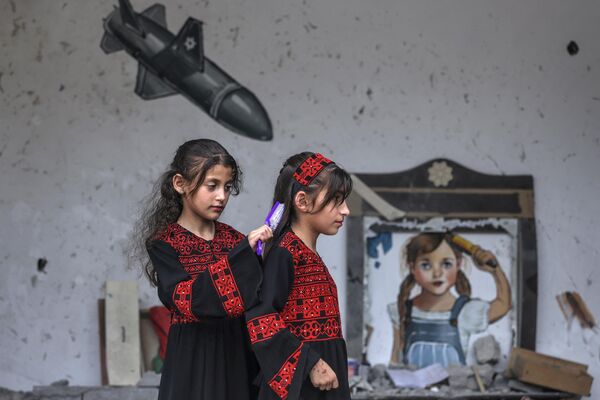 Los residentes de la ciudad de Deir al-Balah, en el centro de la Franja de Gaza, crearon murales y expusieron fragmentos de misiles israelíes para llamar la atención sobre la destrucción de sus hogares y la muerte de civiles.En la foto: Niñas palestinas delante de un mural en la pared de una de las casas destruidas de la comunidad. - Sputnik Mundo