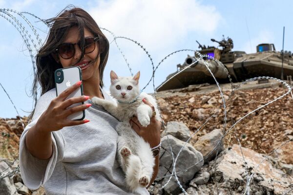 Una mujer hace un selfi con su gato delante de un tanque israelí Merkava cerca de la línea de demarcación entre Líbano e Israel, en la zona del pueblo libanés de Kfar Shuba. - Sputnik Mundo