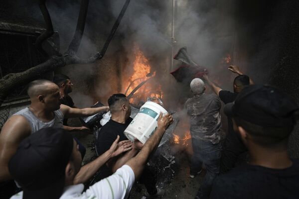 Palestinos extinguen un coche en llamas tras el bombardeo israelí del campo de refugiados de Balata, cerca de la ciudad de Nablus, en la Cisjordania ocupada. - Sputnik Mundo