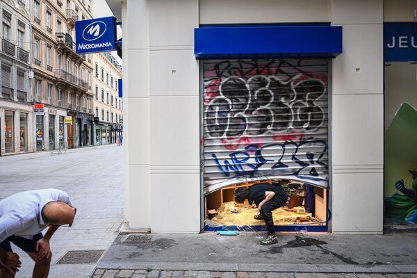 Un cabo de bomberos de 24 años murió en el barrio parisino de Saint-Denis cuando intentaba apagar coches incendiados en un aparcamiento subterráneo. En la foto: un transeúnte y un empleado ante una tienda saqueada en Lyon. - Sputnik Mundo
