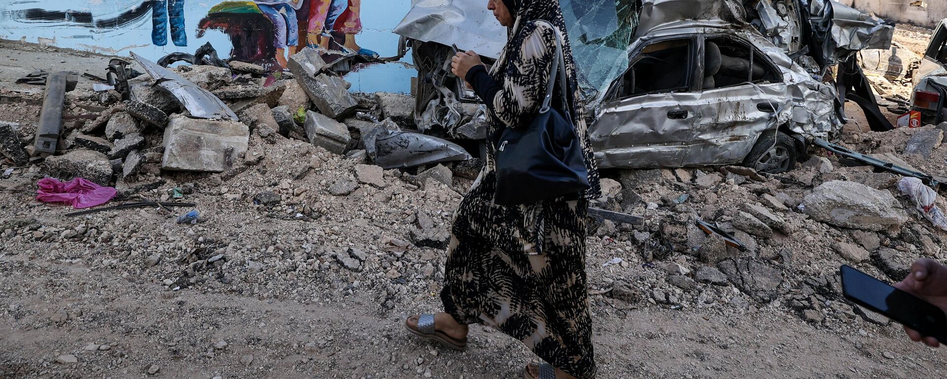 Una mujer pasa junto a los restos de un coche en una calle de la ciudad ocupada de Yenín, en Cisjordania, el 5 de julio de 2023, después de que el Ejército israelí declarara el fin de una operación militar de dos días en la zona.  - Sputnik Mundo, 1920, 07.07.2023