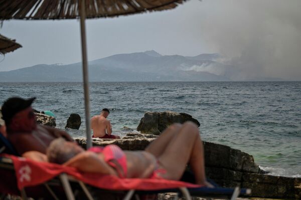 Más de 2.500 turistas fueron evacuados por vía marítima de la isla griega de Corfú.En la foto: turistas en la playa de la ciudad albanesa de Saranda miran el humo de un incendio forestal que se eleva sobre la isla griega de Corfú. - Sputnik Mundo