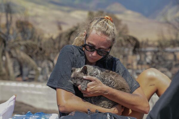Una mujer con un gato encontrado en el lugar de una casa quemada tras el incendio. - Sputnik Mundo