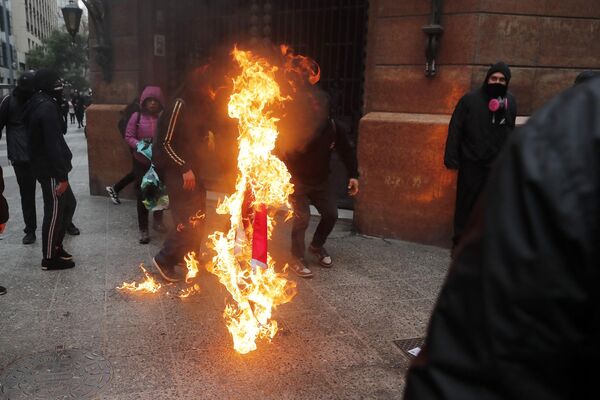 Manifestantes queman una bandera nacional chilena durante una marcha para conmemorar el 50 aniversario del golpe militar liderado por el general Augusto Pinochet. - Sputnik Mundo