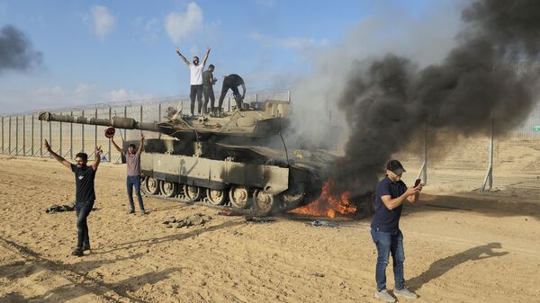 Palestinos celebrando junto a un tanque israelí destruido en la valla de la Franja de Gaza - Sputnik Mundo