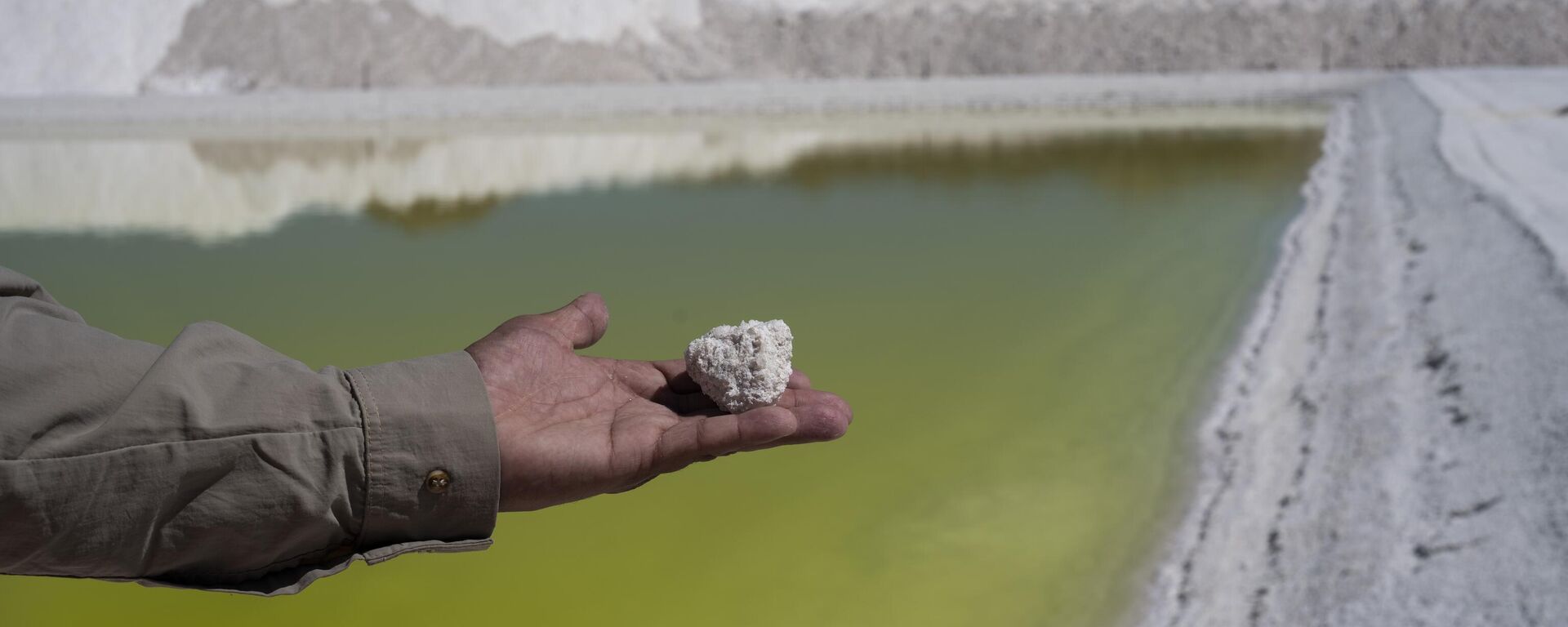 Trabalhador da mina de lítio Albemarle mostra um pedaço de sal perto de uma piscina de salmoura altamente concentrada em lítio no deserto do Atacama, no Chile, segunda-feira, 17 de abril de 2023 - Sputnik Mundo, 1920, 10.11.2023