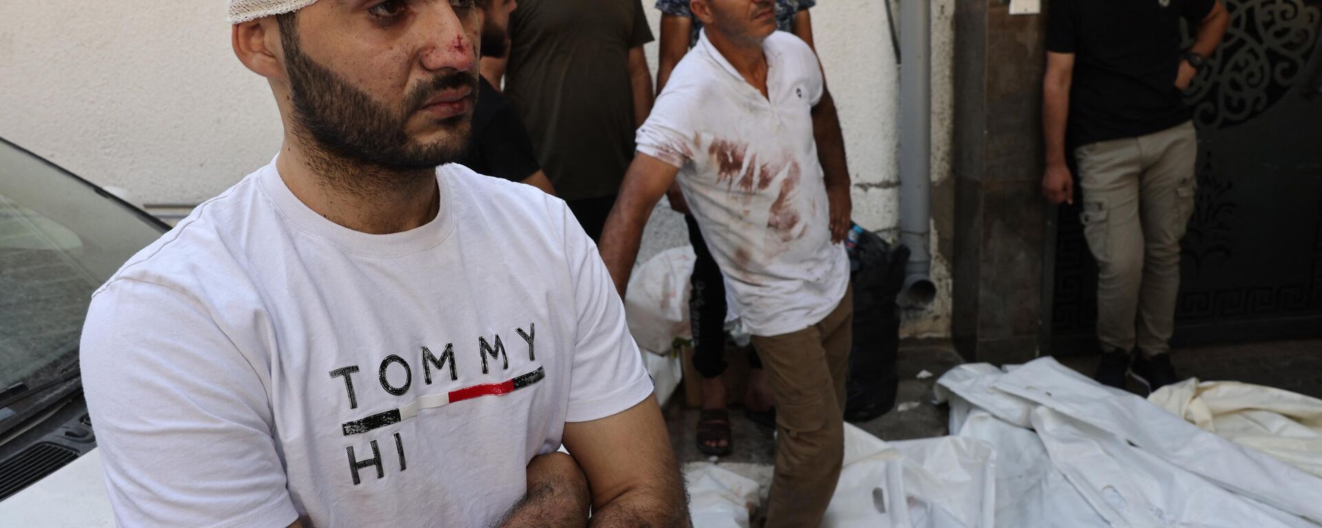 Un palestino herido junto a otras personas junto a los cuerpos de las víctimas de los ataques aéreos israelíes frente al depósito de cadáveres del hospital Al Shifa en la ciudad de Gaza el 12 de octubre de 2023. - Sputnik Mundo, 1920, 15.10.2023