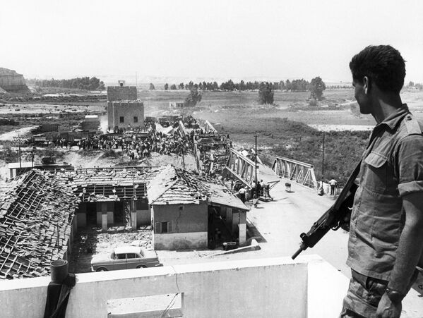 En mayo de 1964 se creó la Organización para la Liberación de Palestina (OLP) como prototipo de Estado palestino. Tres años después, el 5 de junio de 1967, comenzó la guerra de los Seis Días. Egipto, Siria y Jordania desplegaron tropas hacia las fronteras con Israel, expulsaron a las fuerzas de paz de la ONU y bloquearon la entrada de barcos israelíes en el mar Rojo y el Canal de Suez.En la foto: un soldado israelí observa a los refugiados que cruzan a territorio jordano por el destruido puente Allenby, junio de 1967. - Sputnik Mundo