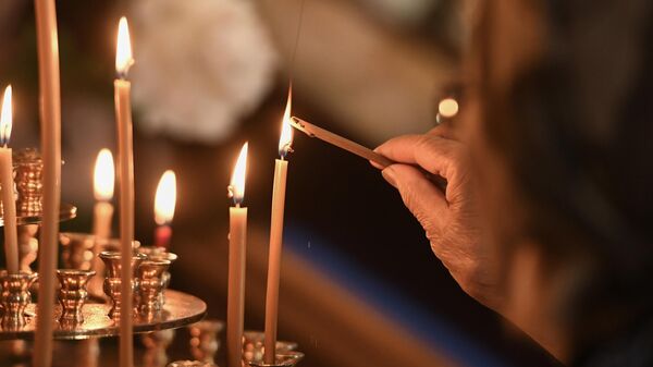 Una mujer coloca una vela de la iglesia durante la Divina Liturgia - Sputnik Mundo