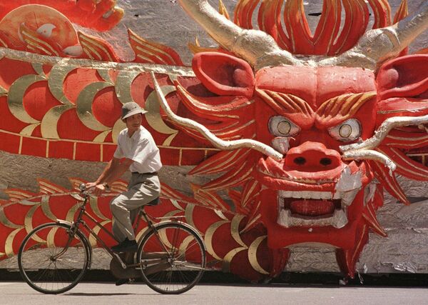 Un hombre en China andando en bicicleta junto a una carroza con cabeza de dragón, que fue parte de la celebración de la reunificación de Hong Kong con China en 1997. - Sputnik Mundo