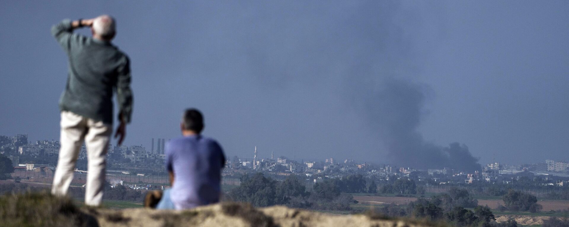 Varias personas observan el humo que se eleva hacia el cielo tras una explosión en la Franja de Gaza - Sputnik Mundo, 1920, 07.01.2024