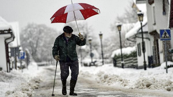 Un hombre se cobija bajo un paraguas mientras camina por una calle cubierta de nieve en Burguete, norte de España, el 16 de enero de 2023  - Sputnik Mundo