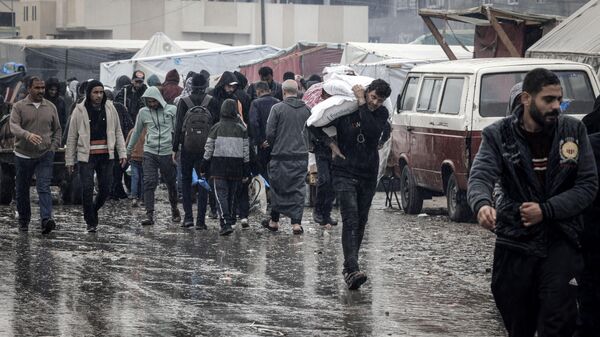 Palestinos caminan bajo la lluvia en un campamento improvisado que alberga a palestinos desplazados, en Rafah - Sputnik Mundo