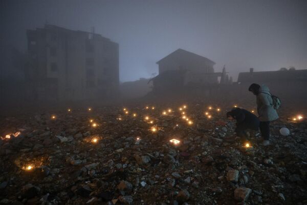 Varias personas ponen velas en el solar de un edificio destruido por el desastre natural en Antioquía. - Sputnik Mundo