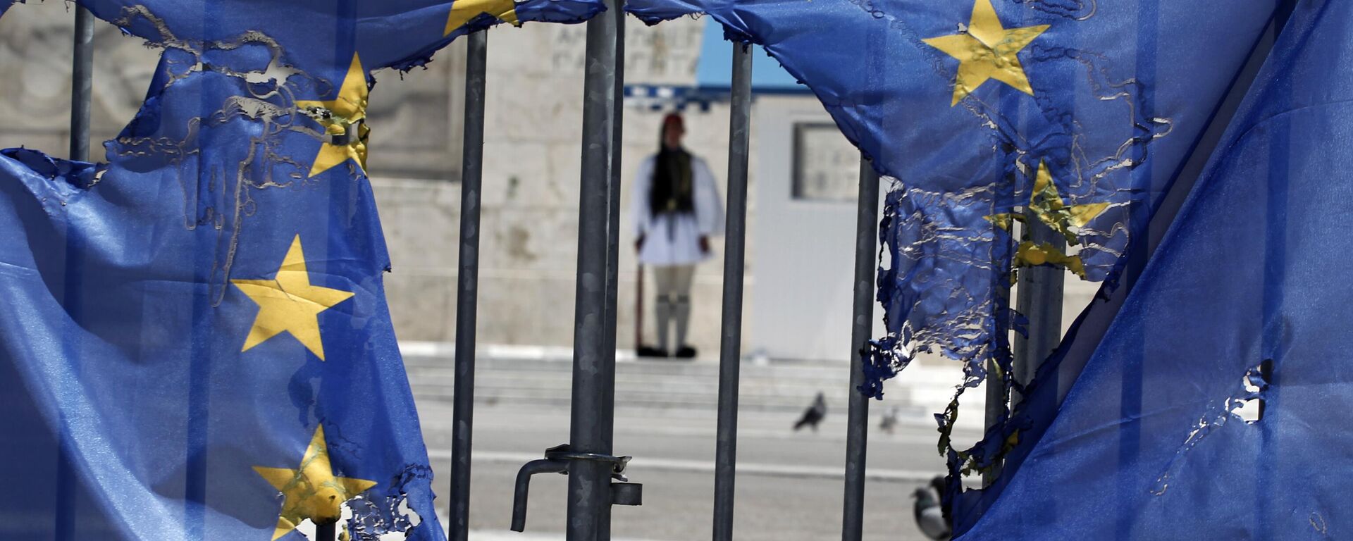 Un guardia presidencial griego permanece enmarcado por los restos de una bandera de la Unión Europea, medio quemada por manifestantes en Atenas, el 1 de mayo de 2013 - Sputnik Mundo, 1920, 30.03.2024