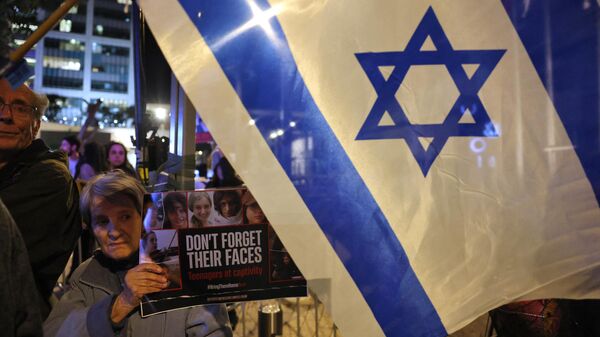 Una mujer sostiene una pancarta con imágenes de los rehenes israelíes retenidos en Gaza desde los ataques del 7 de octubre por militantes palestinos de Hamás, mientras familiares y simpatizantes marchan durante una manifestación que pide su liberación en Tel Aviv, el 15 de febrero de 2024. - Sputnik Mundo