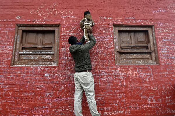 Un niño, sostenido por su padre, escribe un mensaje con tiza en la pared del templo de Saraswati en Katmandú, Nepal, en el festival hindú de Vasant Panchami. - Sputnik Mundo