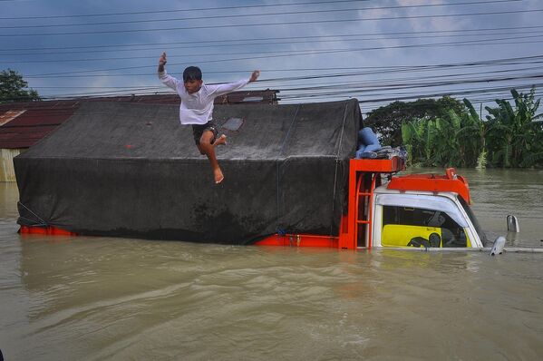 Un niño salta a las aguas que inundaron una carretera debido a las fuertes lluvias y al desbordamiento de un río, en Demak, provincia de Java Central, Indonesia. - Sputnik Mundo