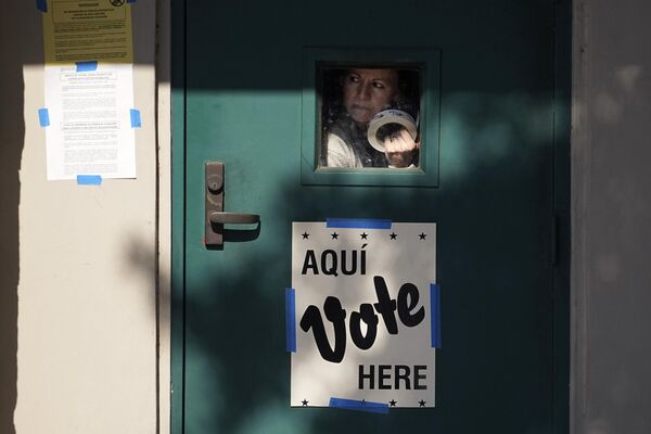Una mujer con un rollo de pegatinas de &quot;He votado&quot; mira por la ventanilla de la puerta de un colegio electoral estadounidense en San Antonio. - Sputnik Mundo