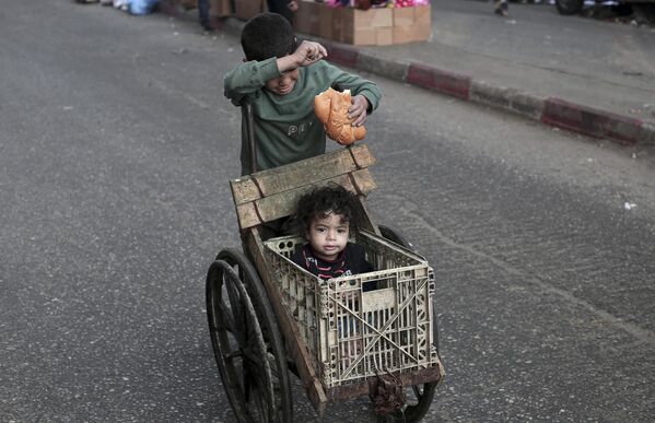 Un niño empuja a otro en un cochecito improvisado en Rafah, en el sur de la Franja de Gaza. - Sputnik Mundo