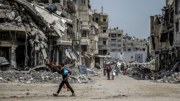 Un niño caminando con bolsas de alimentos cerca de edificios destruidos en la ciudad de Gaza, el 27 de marzo de 2024. - Sputnik Mundo